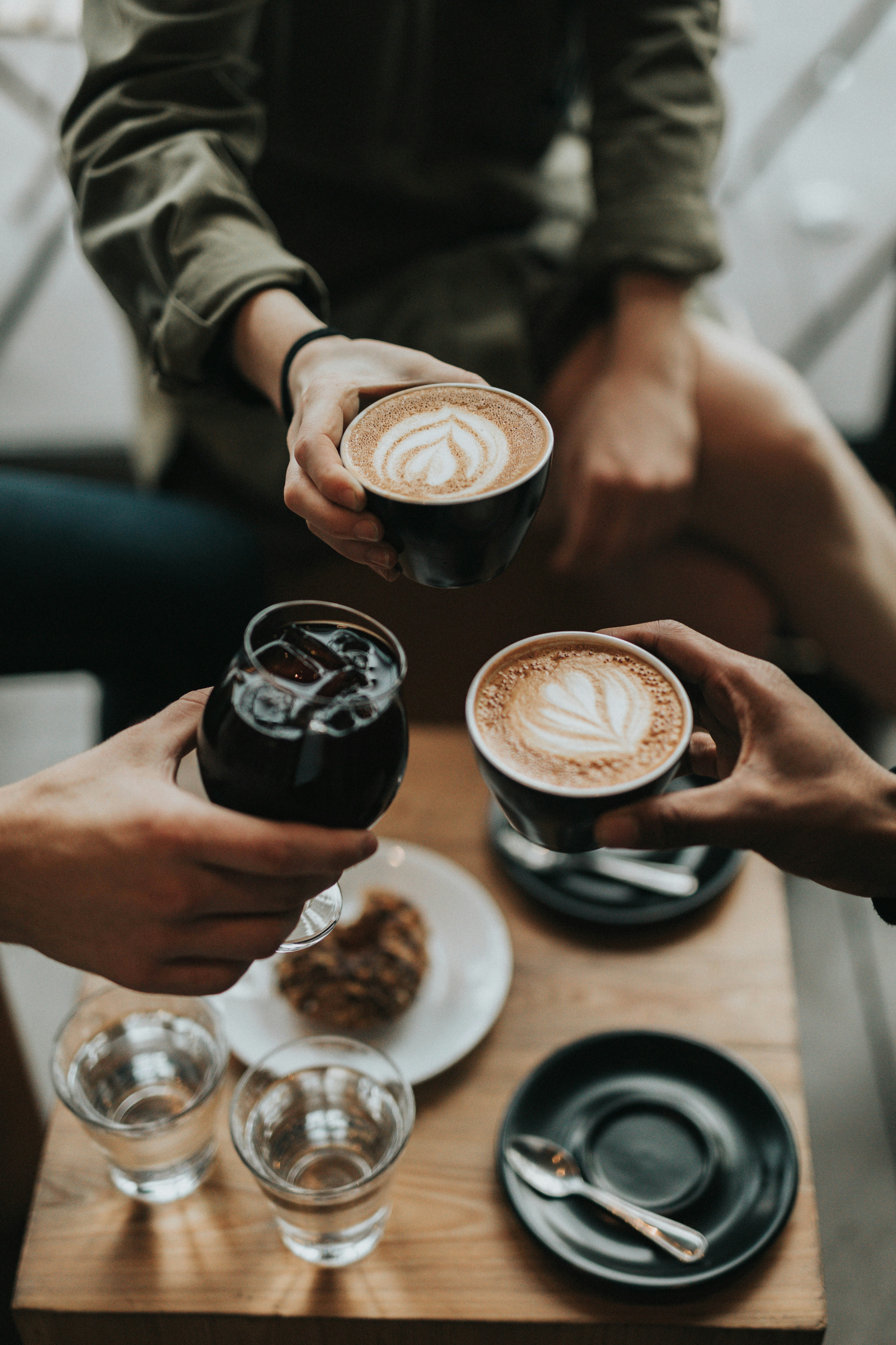 Two people holding cappuccinos with latte art at a café table with pastries
