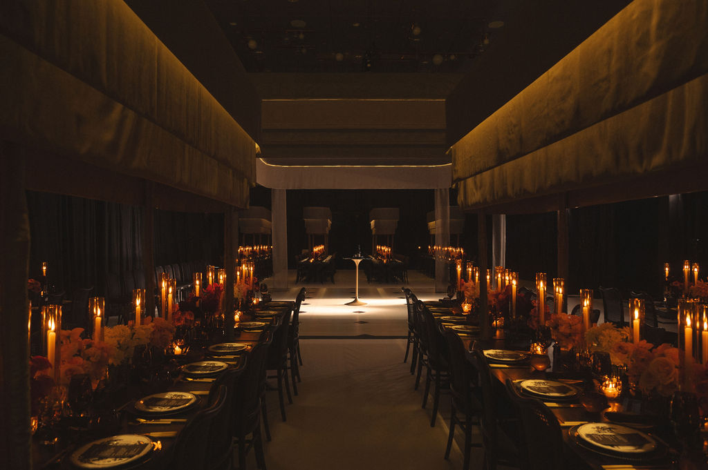 Elegant indoor wedding reception with long wooden tables, floral centerpieces, candles, and hanging greenery.