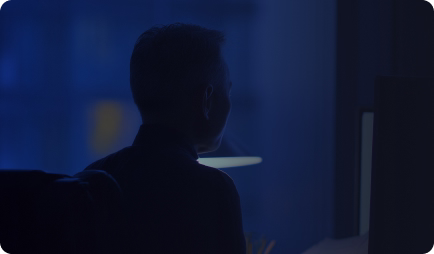 Silhouette of a person sitting in front of a computer screen in a dimly lit room at night.