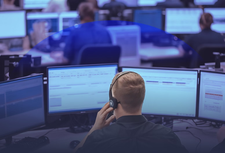 Person wearing a headset working at a computer desk with multiple monitors in an office.