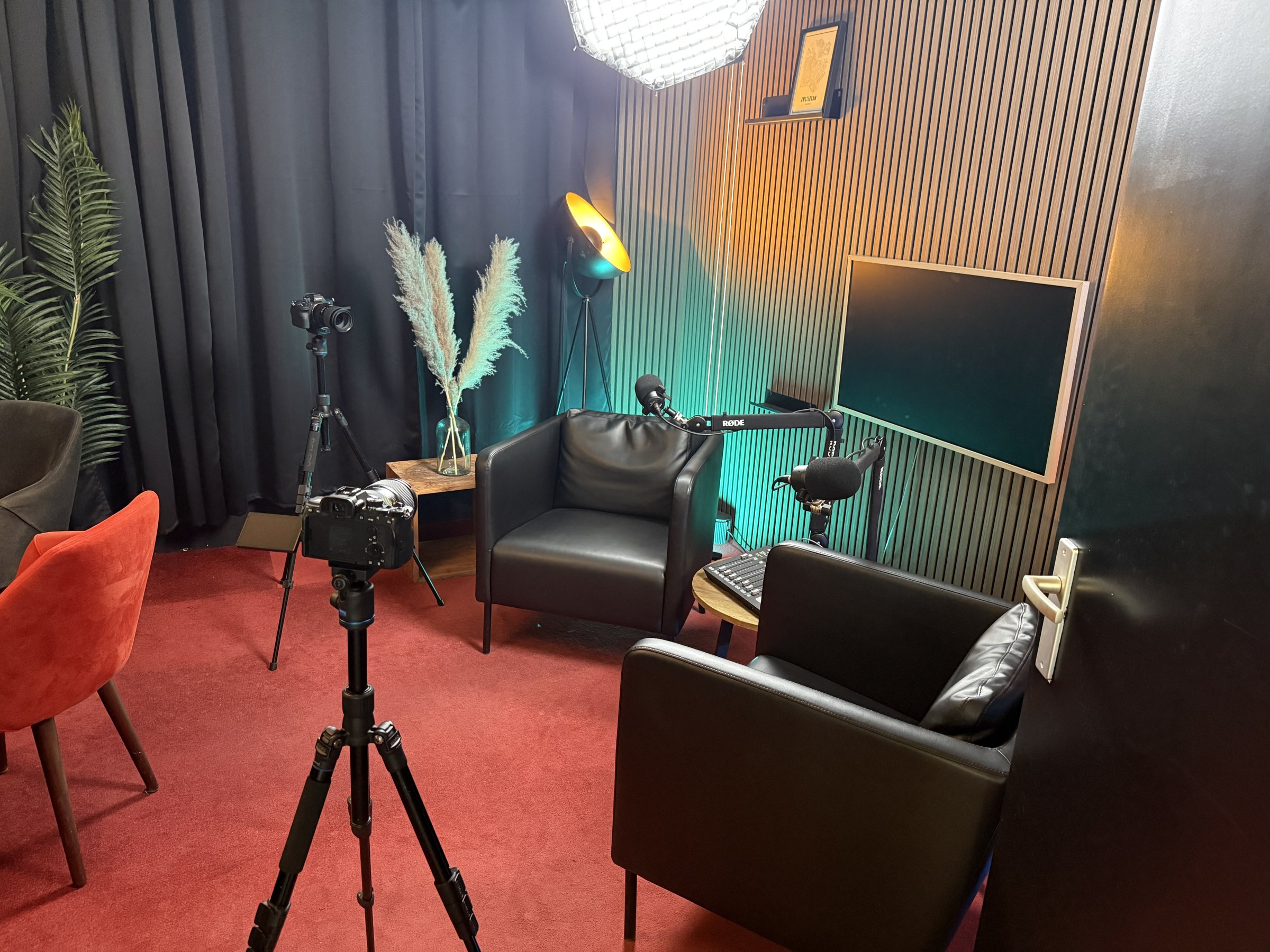 Red Panda Studio podcaststudio in Amsterdam met twee leren fauteuils, RØDE-microfoons, camera's en sfeerverlichting