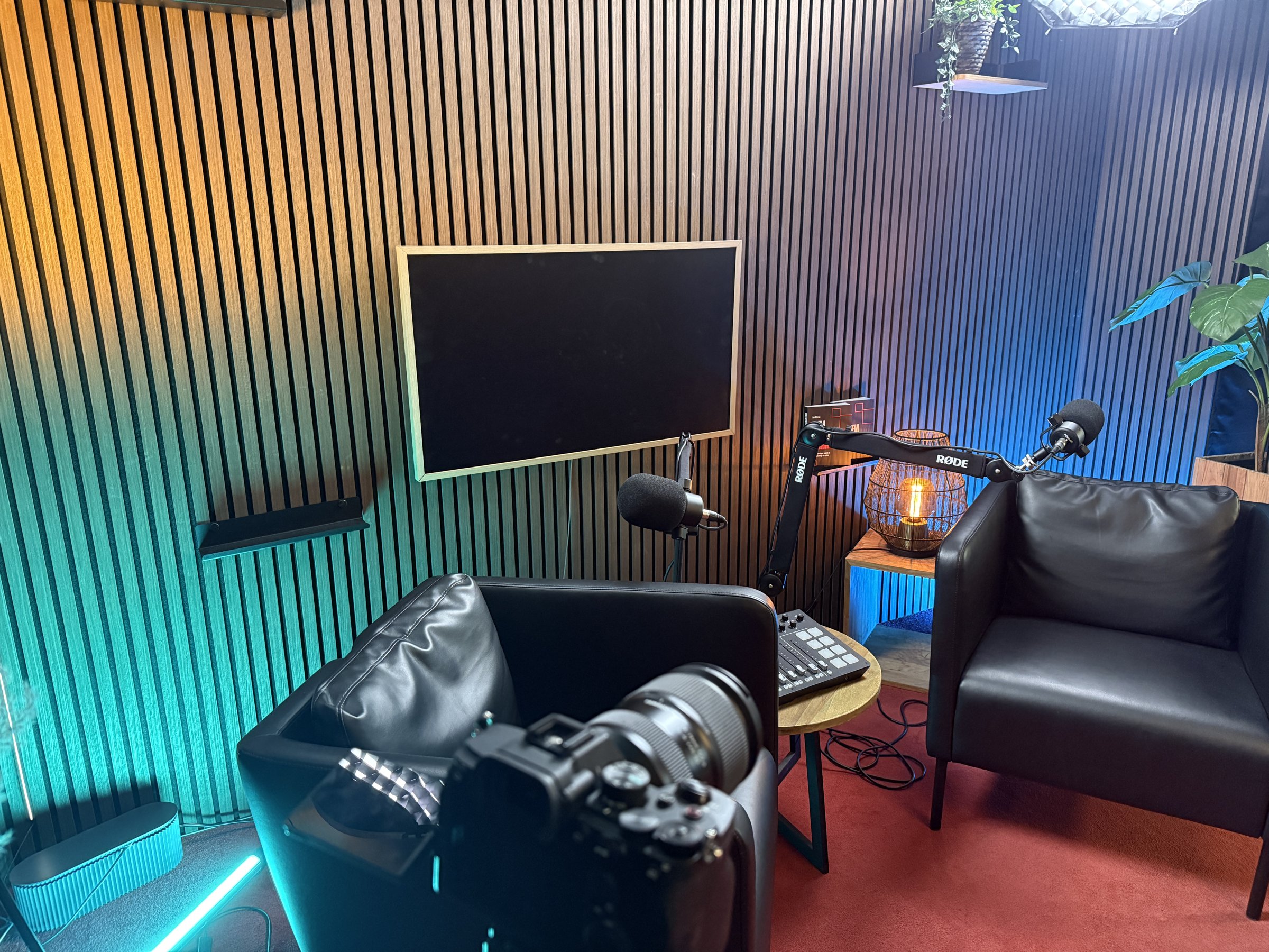 Opstelling in Red Panda Studio met houten akoestische wand, twee microfoons, mixer en camera