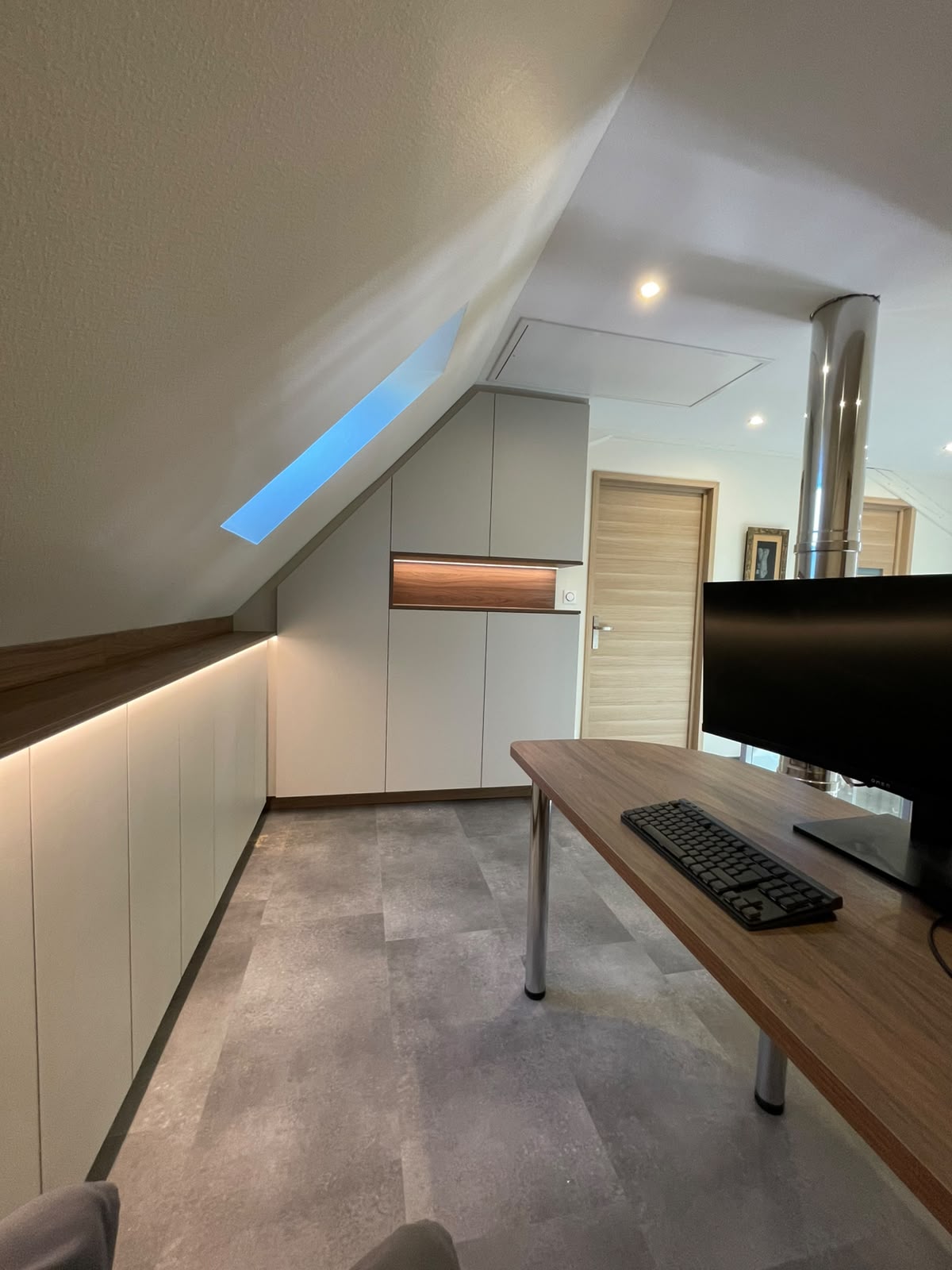 Un bureau sous les toits qui allie style et praticité. L'agencement sur mesure de cette pièce maximise chaque centimètre disponible. Le mélange de matériaux, le bureau design et l'armoire avec sa niche éclairée créent une ambiance feutrée et inspirante pour travailler en toute sérénité.