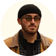 Man wearing a black beanie, sunglasses, and layered brown and black jackets.