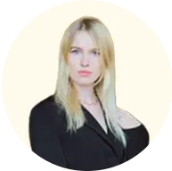 Portrait of a blonde woman wearing a black blazer with a neutral expression against a light circular background.