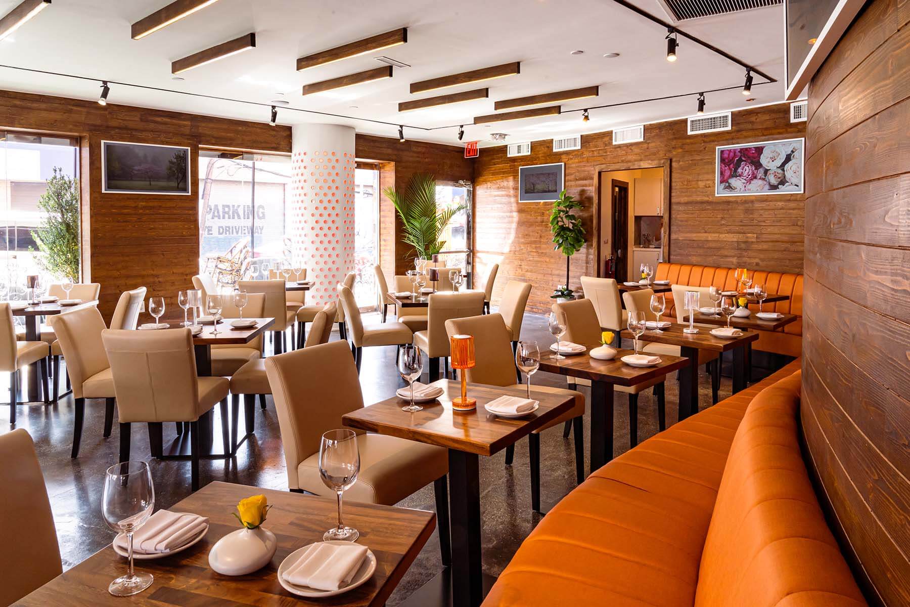 Warm dining room interior at Agenda Restaurant and hookah lounge in Astoria, Queens, featuring wood-paneled walls, orange booth seating, and an open, well-lit space set for dinner service.
