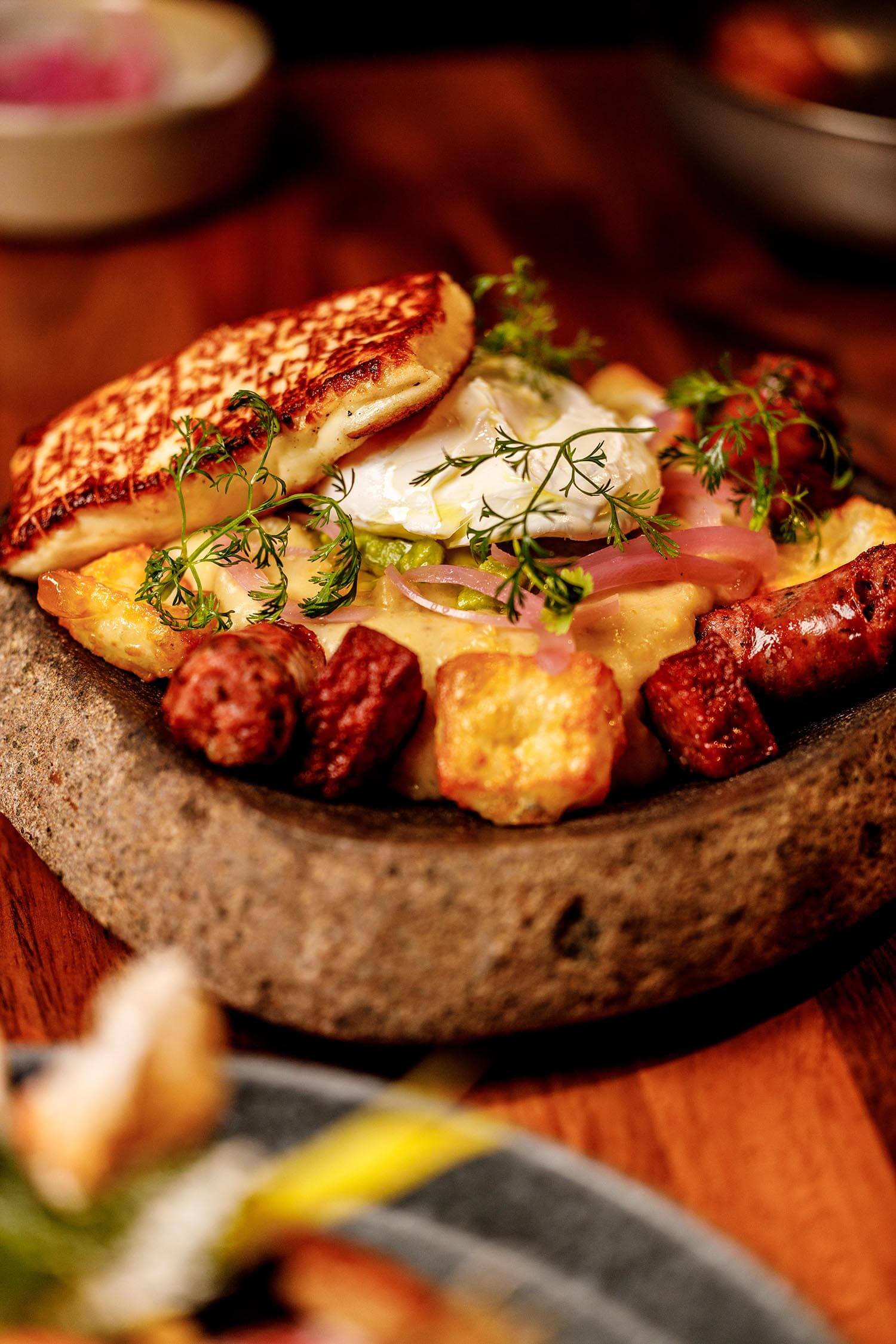 14:00Claude responded: A hearty brunch dish at Agenda Restaurant and hookah lounge in Astoria, Queens, featuring a stone bowl filled with grilled sausage, roasted potatoes, a fried e…A hearty brunch dish at Agenda Restaurant and hookah lounge in Astoria, Queens, featuring a stone bowl filled with grilled sausage, roasted potatoes, a fried egg, and fresh herbs.