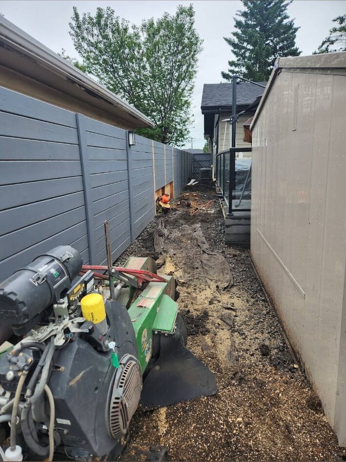 Stump grinder positioned in a narrow backyard access route between a fence and shed in Calgary.