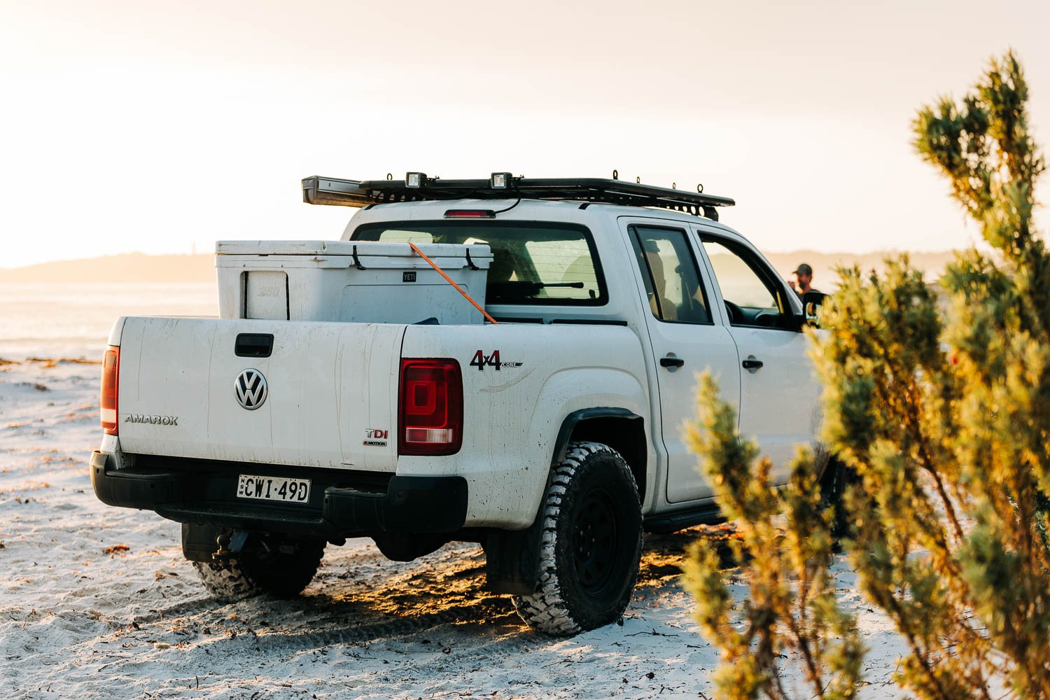 A white ute on the beach at sunset with a YETI hard cooler strapped in the tray