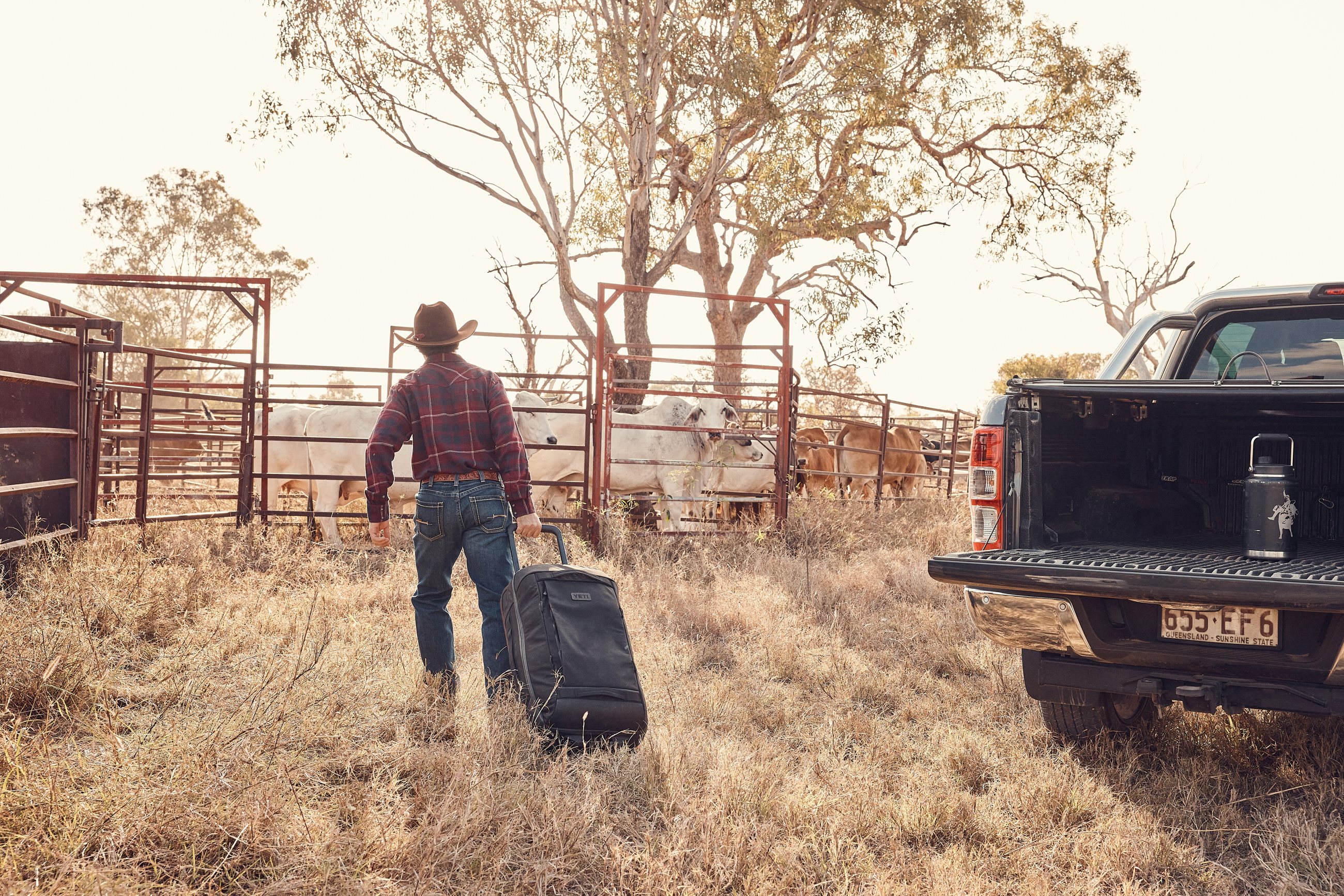 A man in a hat lifting a YETI bag onto a ute tailgate in dry paddock at dusk