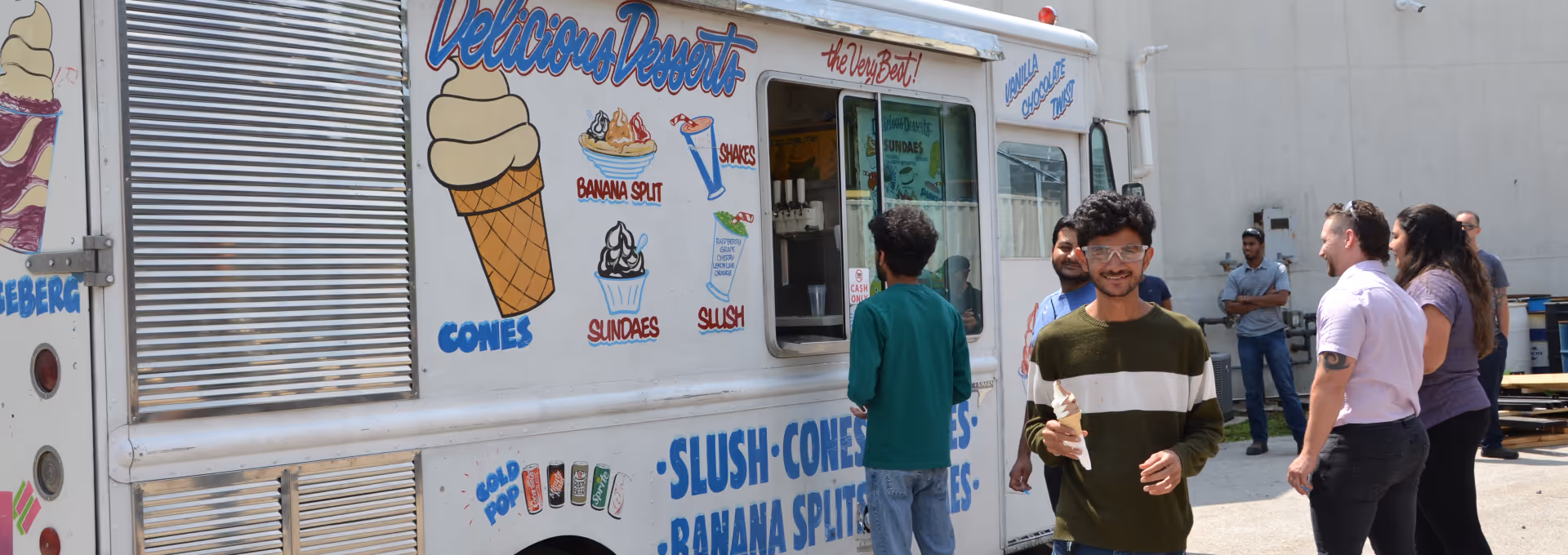 People standing outside an ice cream truck with colorful dessert illustrations and a man smiling holding an ice cream cone.