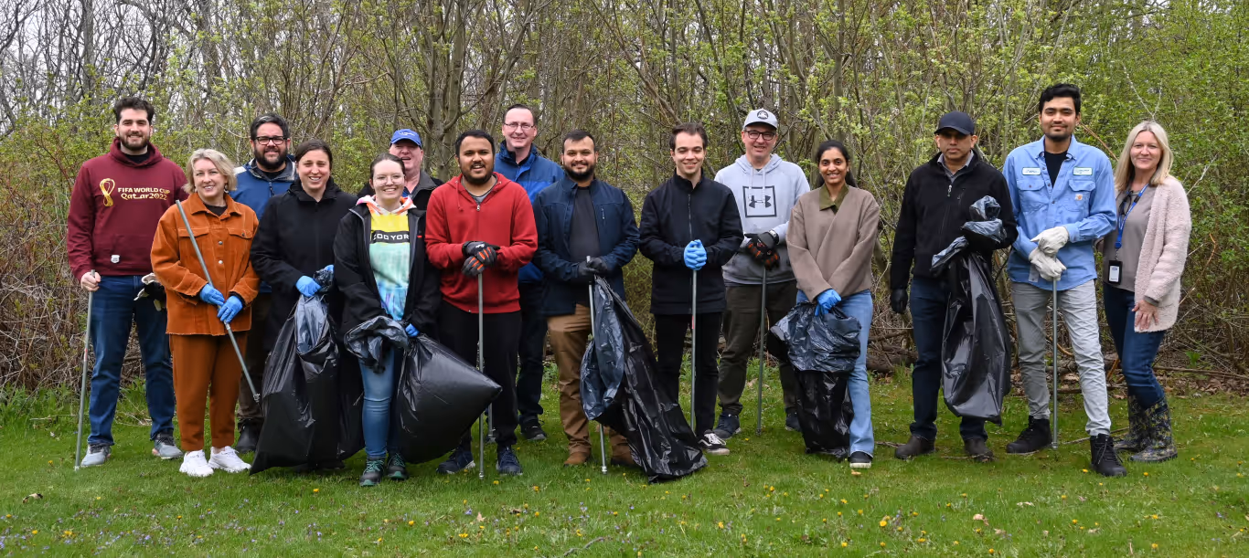 Group of people standing outdoors holding trash bags and picker tools for a community cleanup.