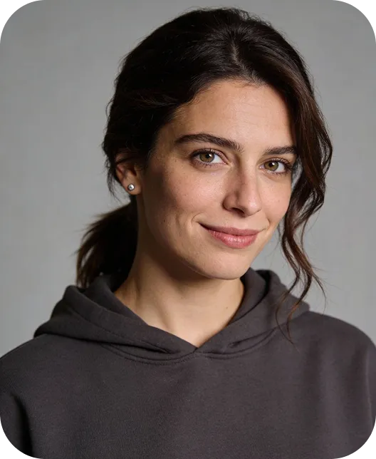 Young woman with brown hair pulled back, wearing pearl earrings and a dark hoodie, smiling softly against a gray background.