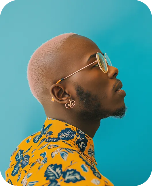 Profile of a man with light pink hair, round glasses, floral yellow shirt, and earrings against a blue background.