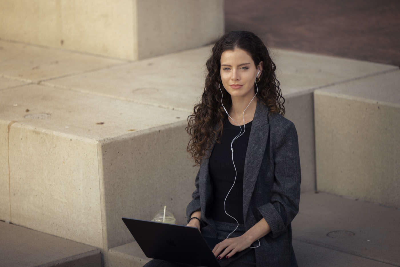 Student with a laptop and earphones sitting on sandstone steps