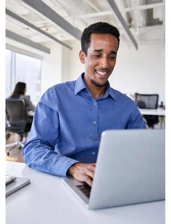 A man in a blue shirt typing on a laptop in a modern office