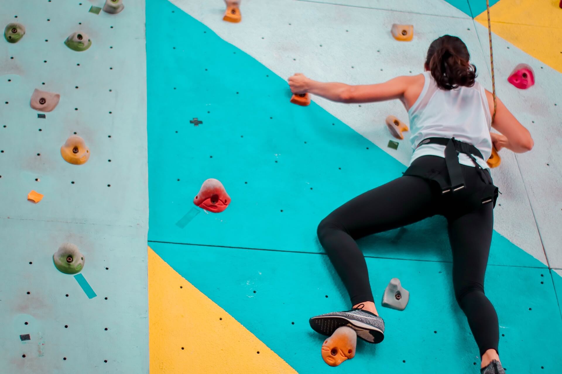 woman in white t-shirt and black leggings Climbing In Gym with safety gear on
