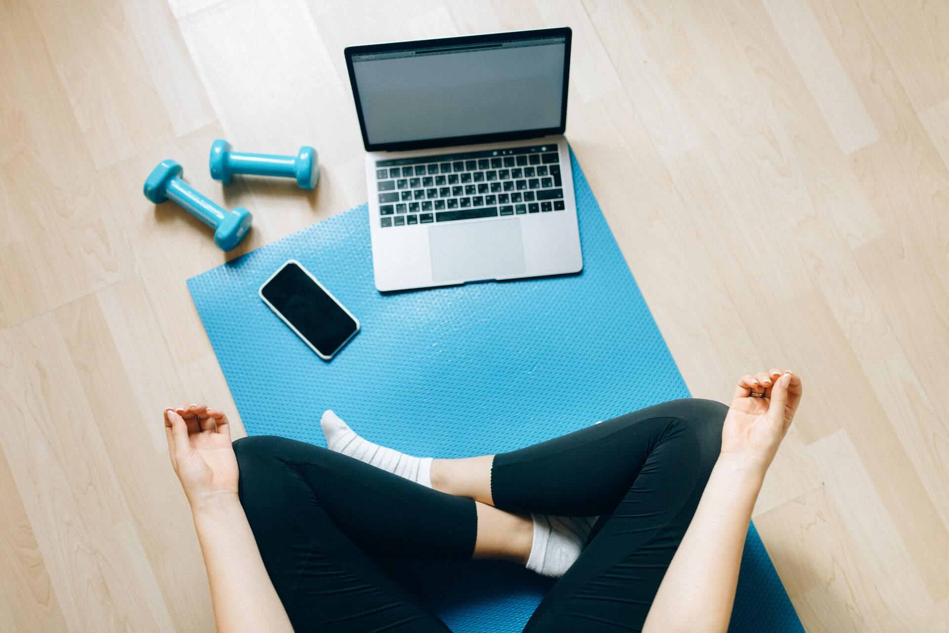 A women in Black Pants Sitting on Yoga Mat and looking at a laptop