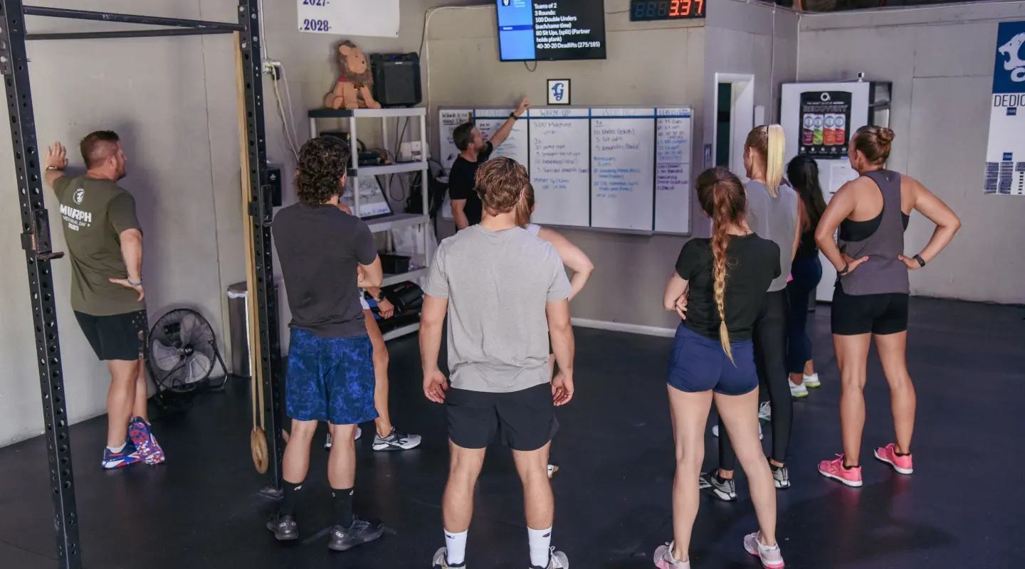 A fitness coach briefing a group of participants on the daily workout using a digital screen and whiteboard during a drop-in class at Graham Fitness in Neptune Beach, FL.