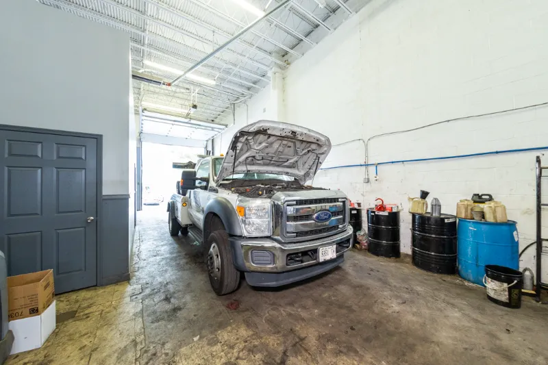Ford tow truck in repair bay with hood open, surrounded by oil drums and service equipment.