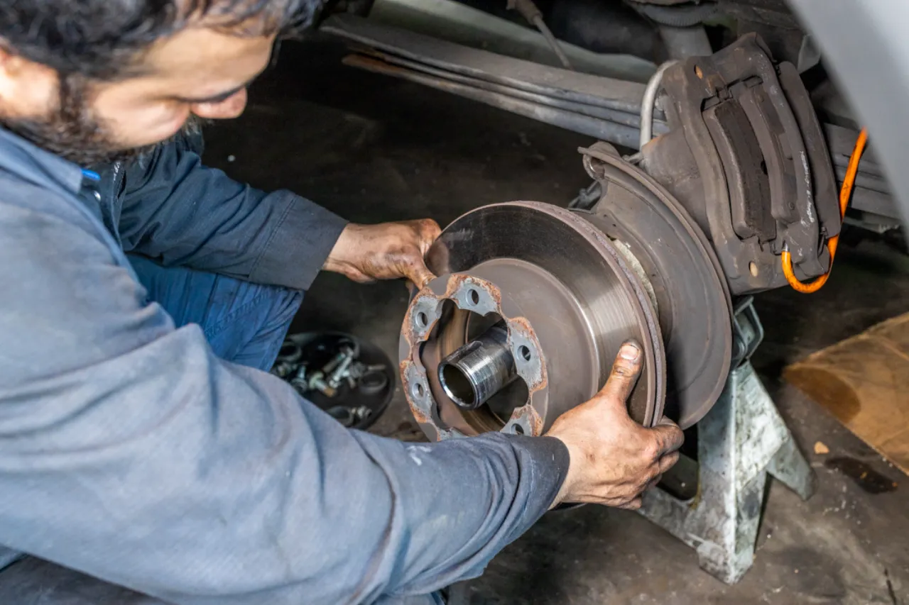 Mechanic removes rusted brake rotor during heavy-duty brake service, showing worn pads and the exposed hub.