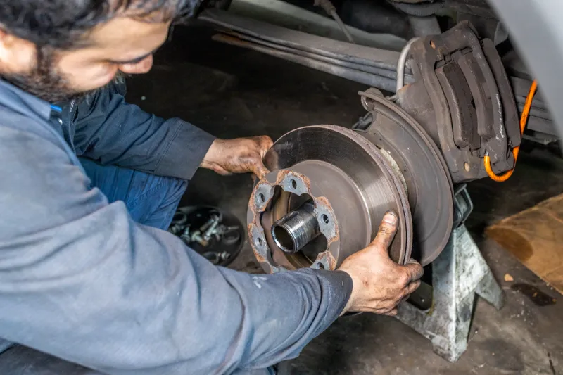 Mechanic removes rusted brake rotor during heavy-duty brake service, showing worn pads and the exposed hub.