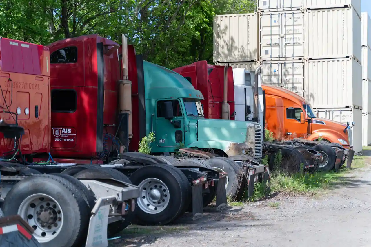 Fleet service for heavy-duty trucks, showing several semi tractors parked beside stacked shipping containers in an outdoor yard.