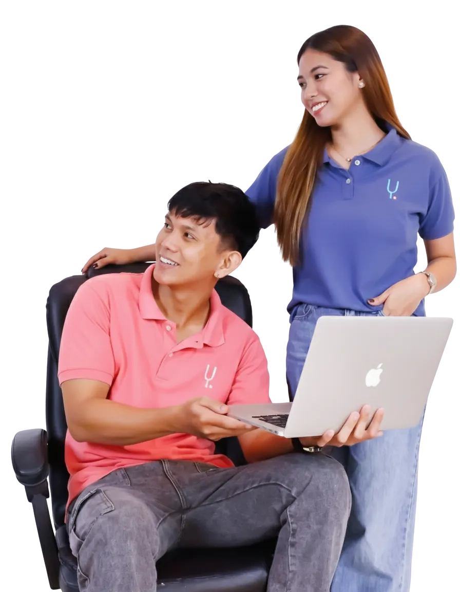 Two smiling coworkers, a man and a woman, look at a laptop together.