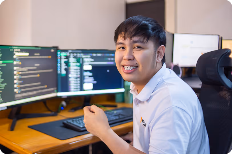 Smiling man in a white polo shirt sitting at a desk with two computer monitors.
