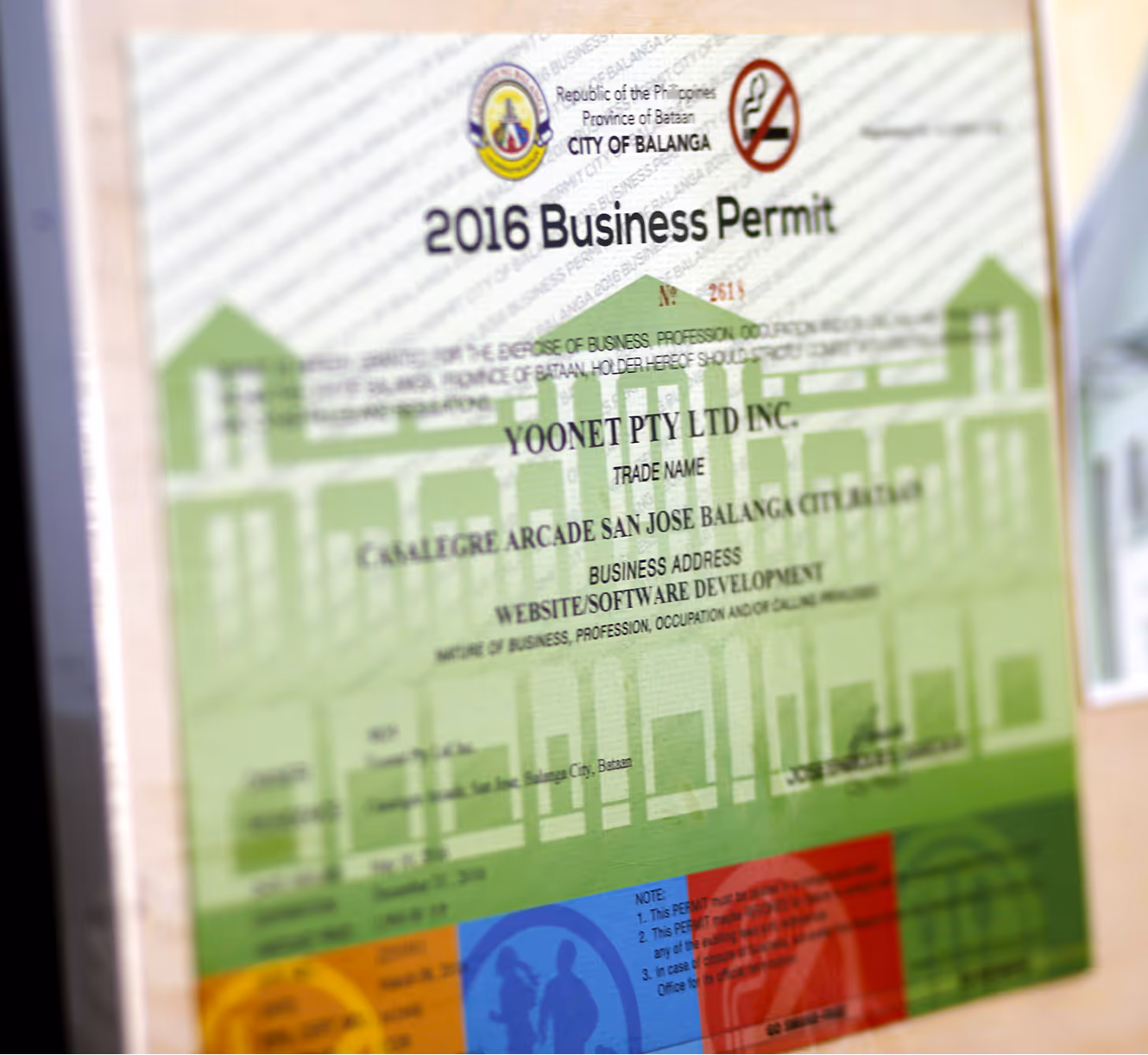 A framed 2018 Business Permit from the City of Balanga with green building graphics.