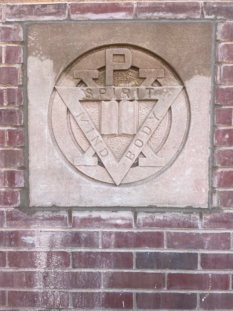 The YMCA seal (Spirit, Mind, Body) from above the doors of Illini Hall, the Y's 1908 building, set into the wall of 1001 S. Wright St. in November 2023. University YMCA.