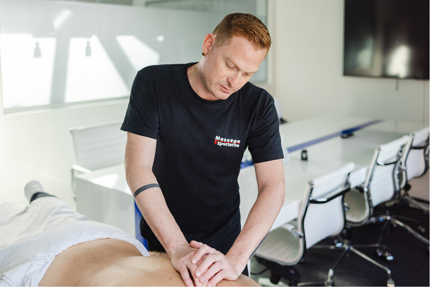 Massør fra Massage Experterne giver professionel rygmassage til medarbejder i lyst mødelokale som del af firmamassage.