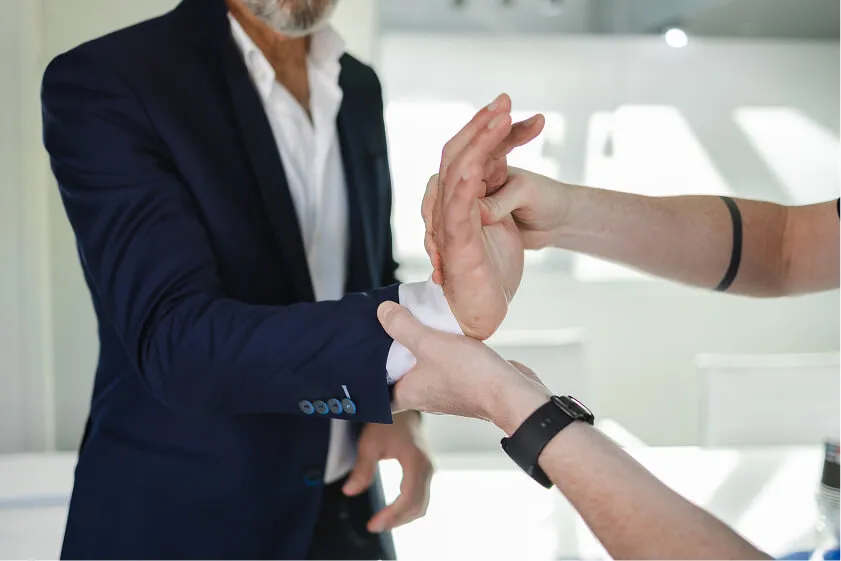 Massør vurderer bevægelighed i medarbejders hånd og underarm under konsultation på kontoret.