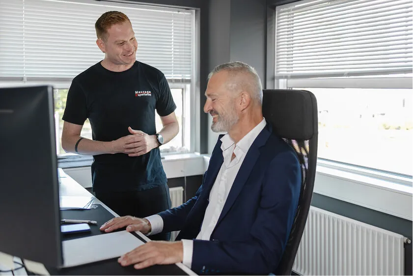 Massør taler med medarbejder om ergonomi og spændinger ved computeren i forbindelse med firmamassage.