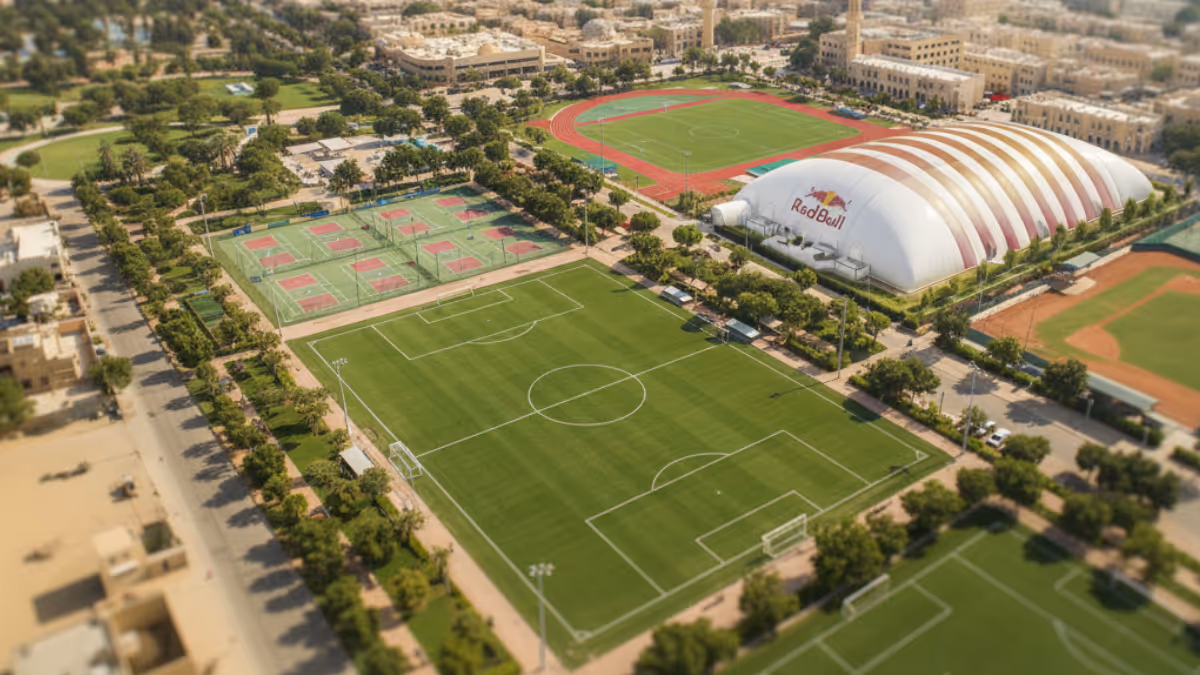 Aerial view of a sports complex with a soccer field, multiple tennis courts, a Red Bull branded dome, a running track, and a baseball field surrounded by trees and buildings.