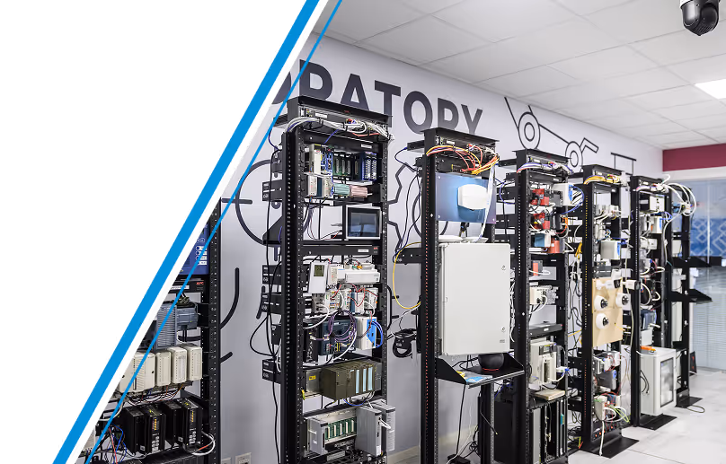 A room, likely a laboratory or training facility, is filled with numerous black metal racks. Each rack is densely packed with various electronic components, including circuit boards, processors, and other hardware.