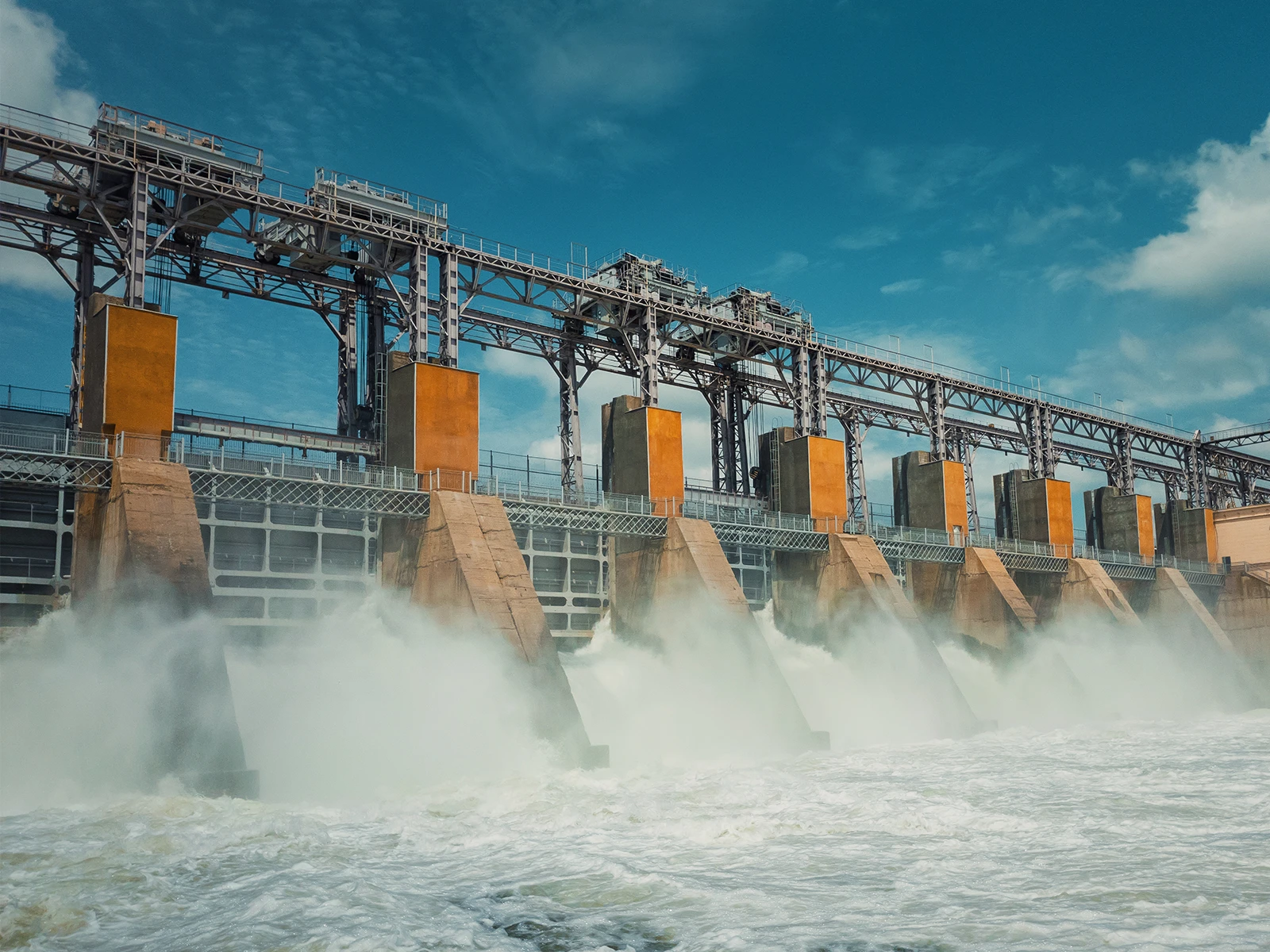 青空の下、複数の放水路から水が勢いよく流れ落ちる水力発電ダム。