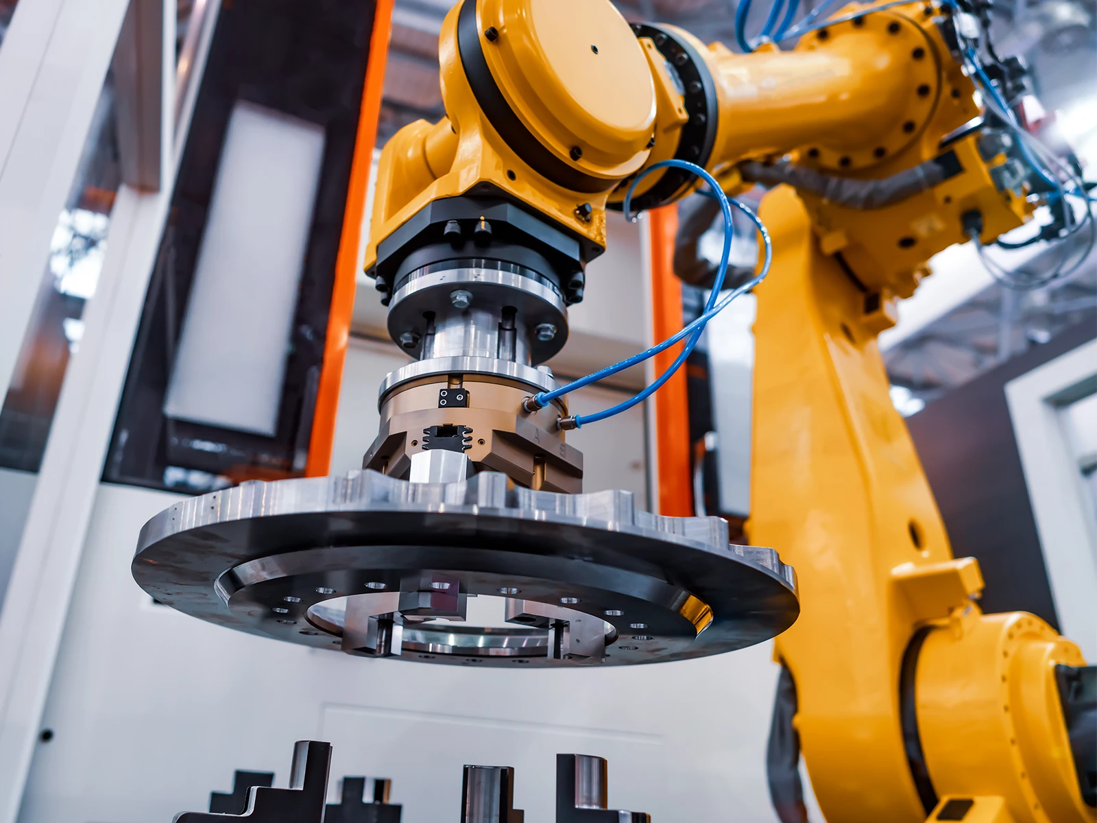 Close-up of a yellow robotic arm holding a large metal gear inside an industrial setting.