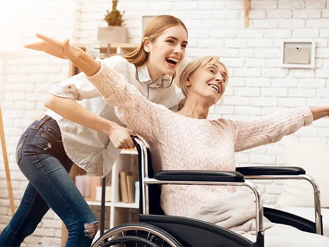 Pflegerin hält einer lachenden Seniorin die Hand