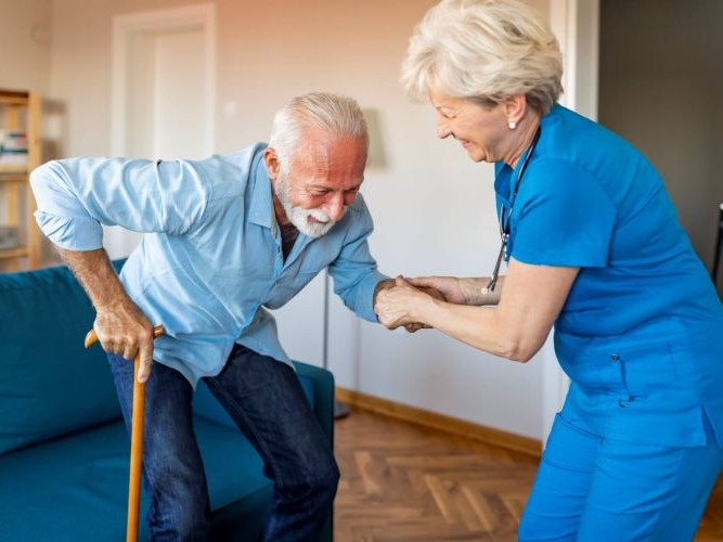 Pflegekraft hilft Senior beim Aufstehen