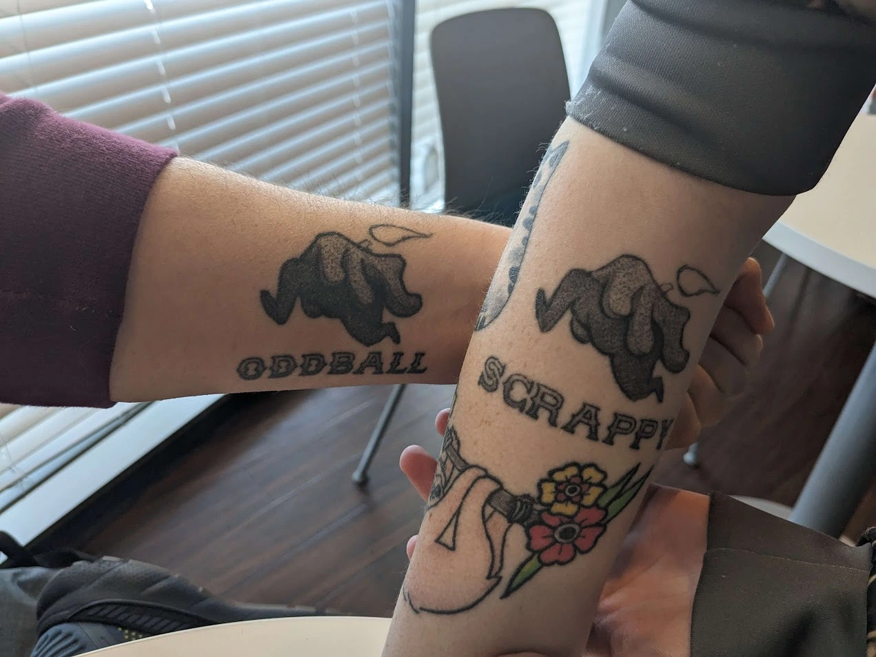 A pair of arms with matching tattoos that say "oddball" and "scrappy" with tattoos shown below a figure that looks like a running candle