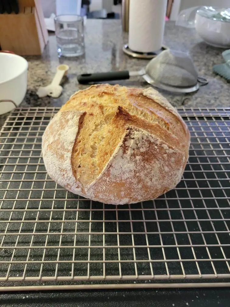 A baked loaf of bread surrounded by kitchen tools