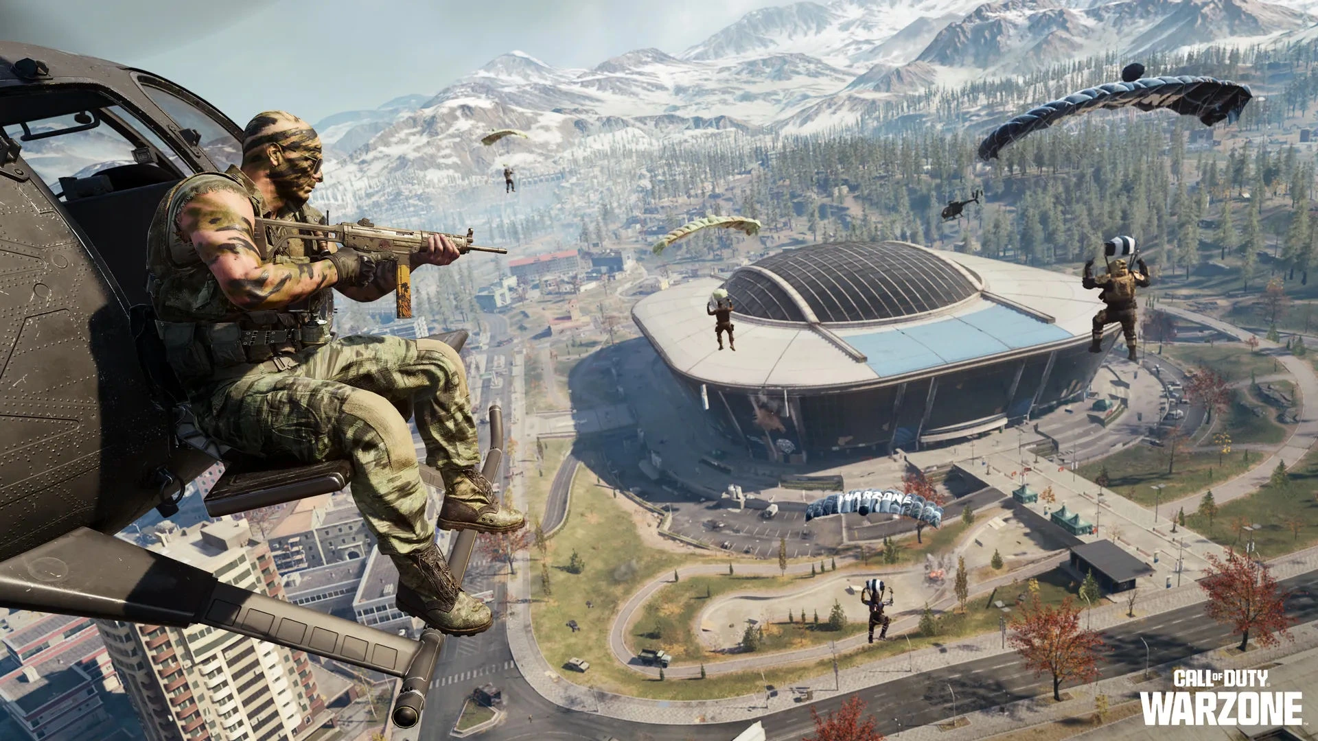 A camouflaged soldier hangs off a helicoptor holding a gun, as other soldiers descend into a Warzone map in Call of Duty