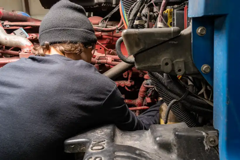 Technician diagnosing a Kubota engine with exposed wiring and hoses in a confined heavy-duty engine bay.