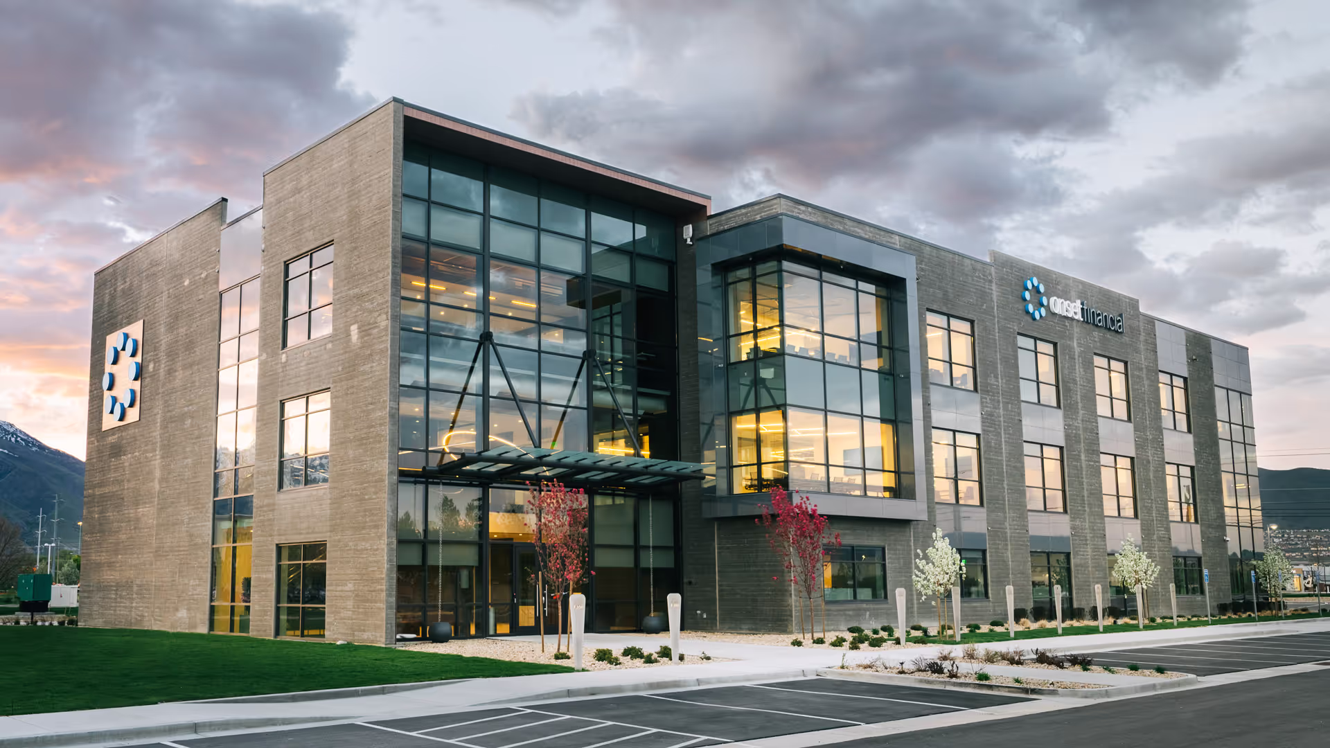 A modern concrete office with dark sunrise clouds in the background. The windows glow yellow with warmth