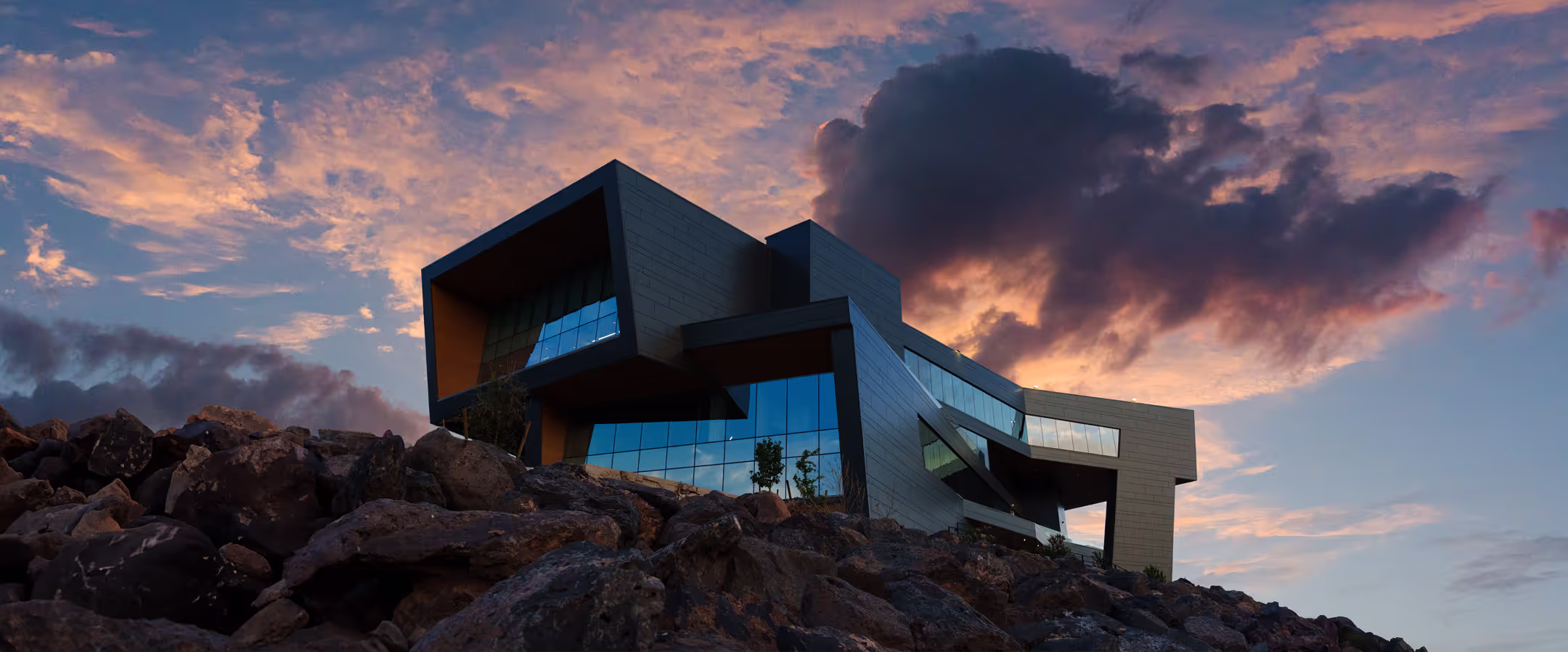 Large futuristic building on top of a rock mountain with a sunset in the background