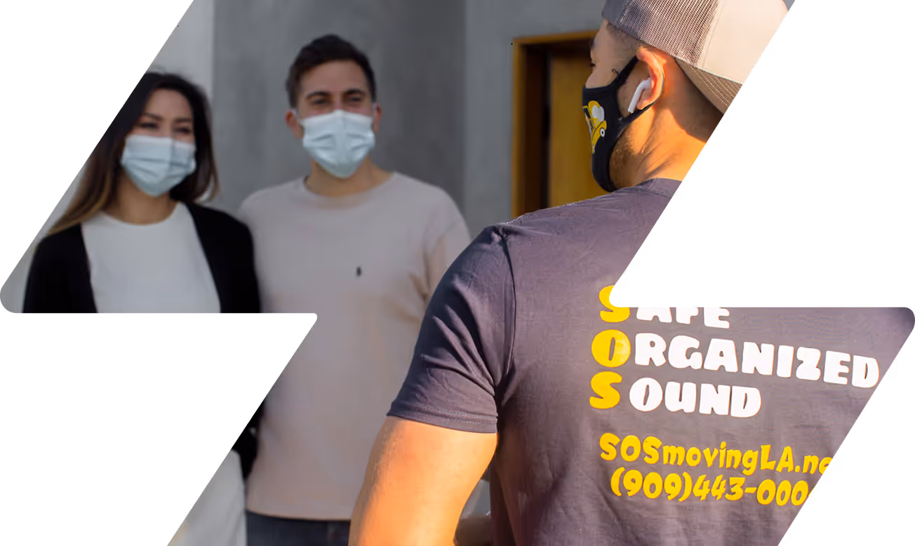 Masked moving company worker in a navy shirt with 'Safe Organized Sound' text faces a masked couple standing near a doorway.