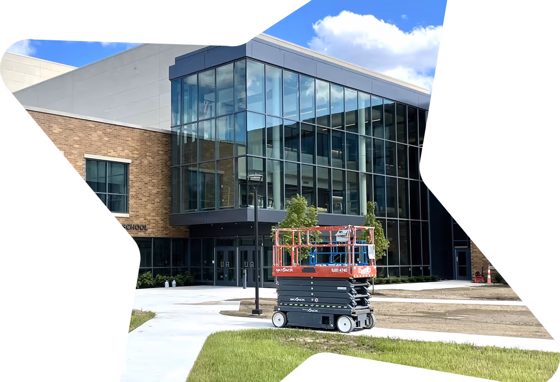 Modern school building with large glass windows and a SkyJack scissor lift parked on the sidewalk outside.