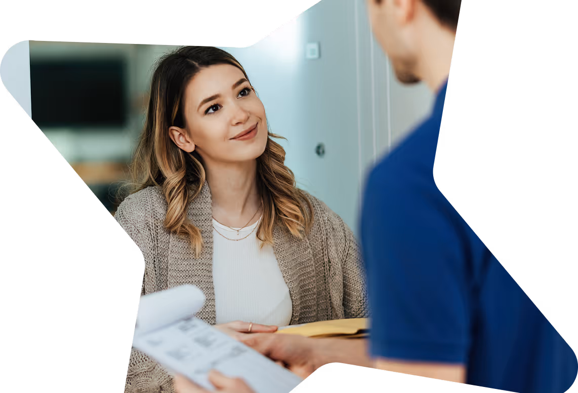 Smiling woman in a beige sweater listening to a man holding a notebook in a home setting.
