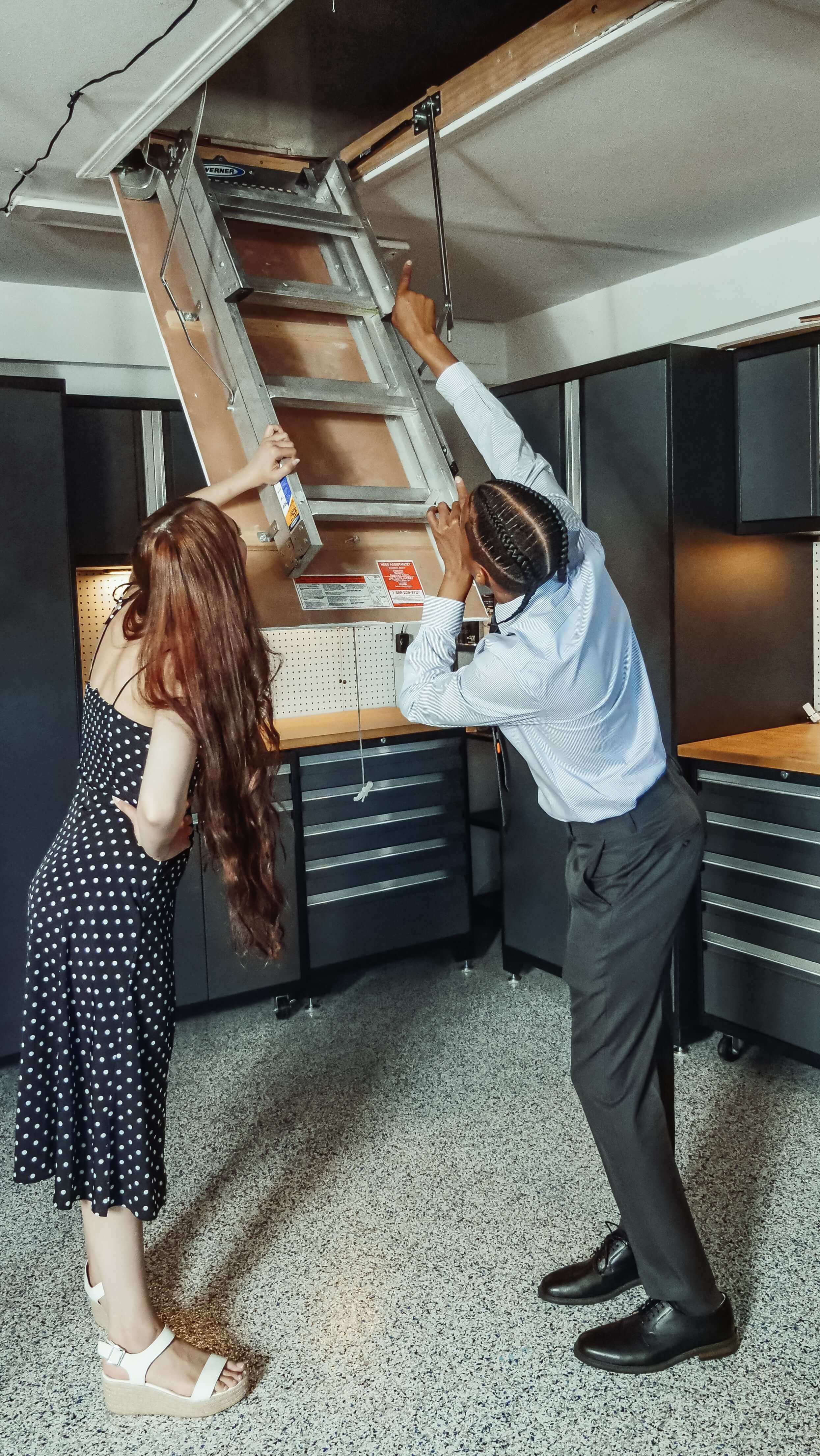 Two people opening a fold-down attic access ladder
